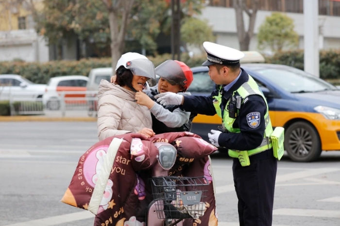 临渭交警指导骑电动车的大人和孩子规范佩戴安全头盔。
